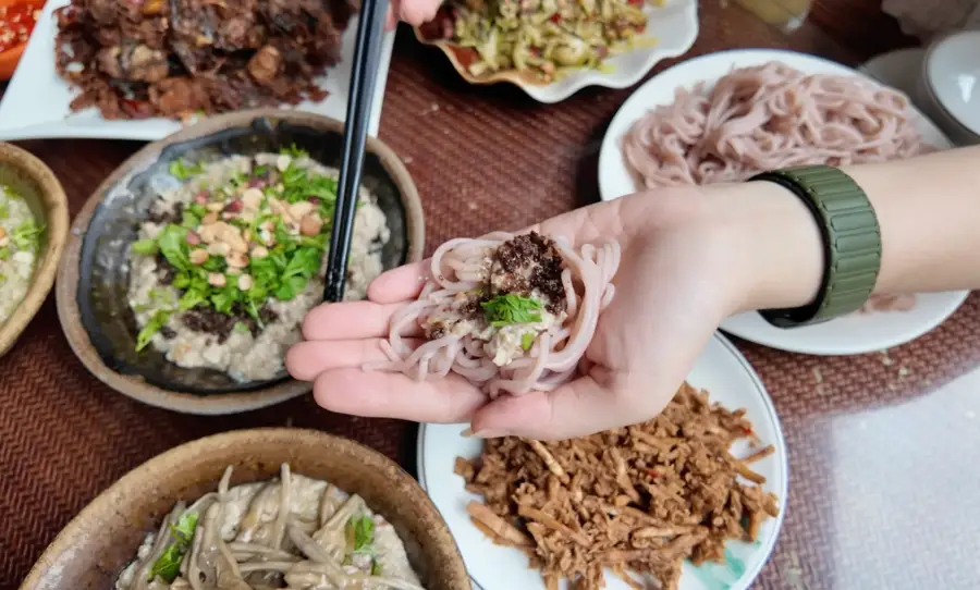 Hand holding rice noodles at a Yunnan table spread