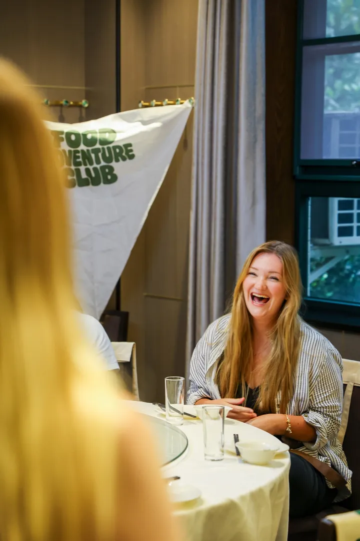 Guest laughing in front of a Food Adventure Club flag
